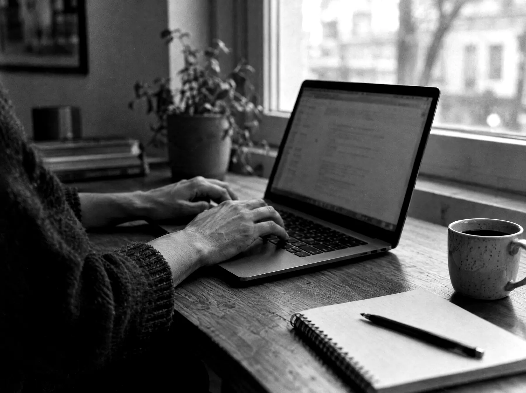 Hands typing on a laptop beside a window
